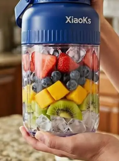 A hand holding a Xiaoks portable blender packed with orange, kiwi and cherries outdoors